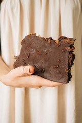 Woman is holding big piece of chocolate with nuts and dried fruits