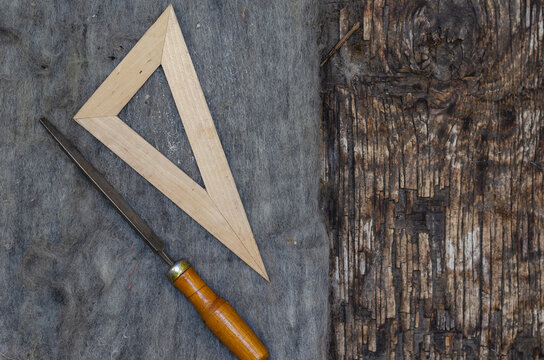 A file and a triangular ruler lie on old felt. Cracked burnt woo