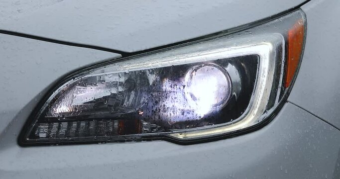A short video of a car's headlight turning on while covered in rain droplets.