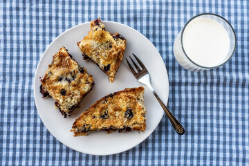 Homemade delicious sliced Apple Blueberry Pie on a white plate and glass of milk on a wooden table with fork and a blue cloth. Top View