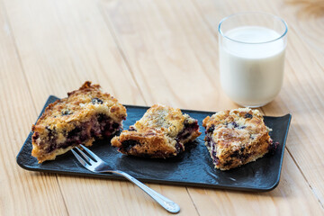 Homemade delicious sliced Apple Blueberry Pie on a black serving plate on a wooden table with a glass of milk