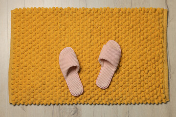 Fototapeta na wymiar Soft orange bath mat and slippers on floor, top view