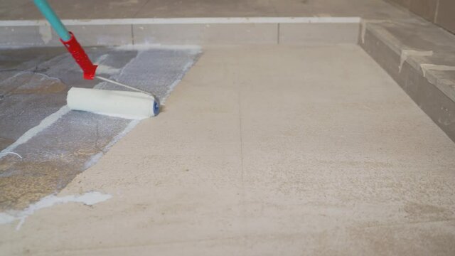 The worker primes the floor with a roller. Parquet worker with paint roller making floor prime coating at home repair renovation work. Finishing works - priming of the floor for the bulk floor.