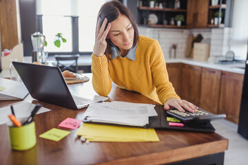 Worried businesswoman working online from home in front of a laptop looking into papers and computer. Stress