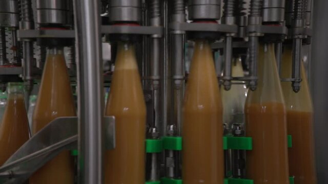 Close up inside of mechanism bottling line filling bottles. Orange-colored sea-buckthorn juice in glass bottles. Pan bottles moving