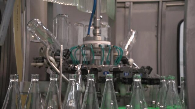 Close up of mechanism bottling line moving and washing empty glass bottles to fill it with sea-buckthorn juice then. Panning up
