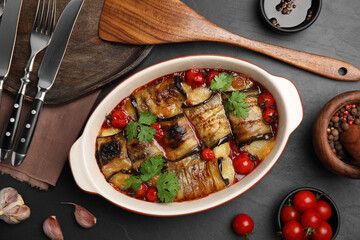 Tasty eggplant rolls with tomatoes, cheese and parsley in baking dish on black table, flat lay