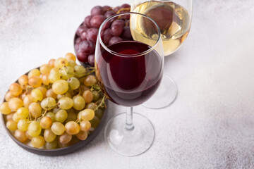 Glasses of white and red wine with ripe grapes on a light stone background