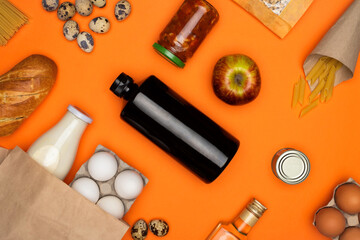 Fototapeta na wymiar Eggs and bottle of milk in paper eco bag. Spaghetti, bread, quail eggs, beans, tomato paste on orange background. Healthy food, delivery, donation concept. Food stock for quarantine. Top view, flatly.