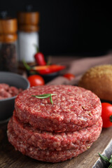 Raw hamburger patties with rosemary on wooden board, closeup
