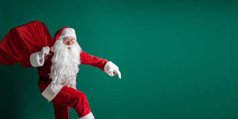 Surprised Santa Claus sneaking while carrying huge red sack with presents on green studio background