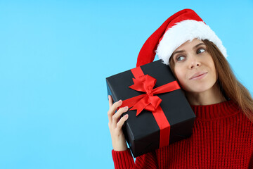Attractive woman in Santa hat holds gift box on blue background