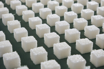 Refined sugar on green background.Cubes of sweet and white sugar in geometricshape. Hard shadows.