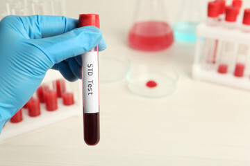 Scientist holding tube with blood sample and label STD Test on blurred background, closeup. Space...