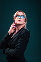 Young caucasian business woman using a mobile phone wearing a black blazer and glasses in a photography studio with a blue dark background.
