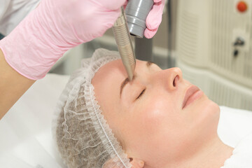 close-up Doctor cosmetologist makes the procedure of laser dermal rejuvenation of the eyelids of the skin around the eyes to the patient. Against the background of a medical office with copy space.