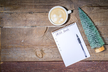 Fototapeta na wymiar 2022 new year goals concept. Year plan and action list on notepad with holiday decoration, latte coffee cup on wooden background flatlay top view copy space
