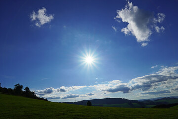 Star-shaped sun. Landscape in the Sauerland with a slightly cloudy sky and green hills.
