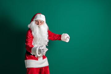 Emotional male actor in costume of Santa Claus with long beard gesturing on green studio background