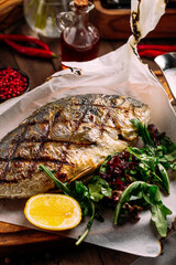Gourmet grilled dorado fish with greens on wooden background