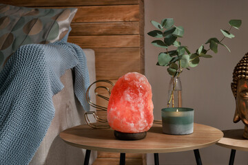 Beautiful Himalayan salt lamp, eucalyptus branches and candle on wooden table in living room