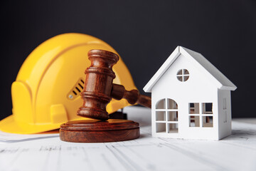 Wooden gavel, house and yellow helmet on construction plan close-up