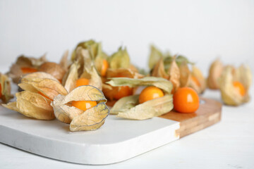 Fototapeta na wymiar Ripe physalis fruits with dry husk on white wooden table. Space for text