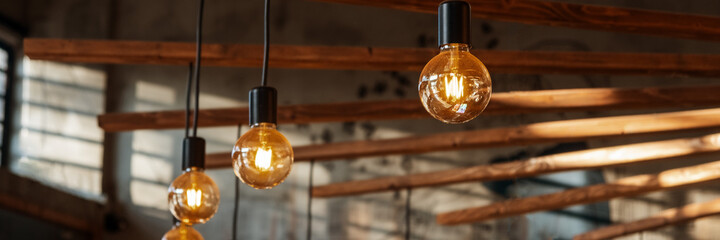 Banner Edison lamps hanging from the ceiling. Vintage style light bulbs decorating room. Loft design background.Antique electronic decorative lamp Retro light lamp decor glowing. 