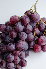 Purple grapes on a white background with drops on the fruits