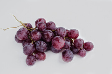 Purple grapes on a white background with drops on the fruits