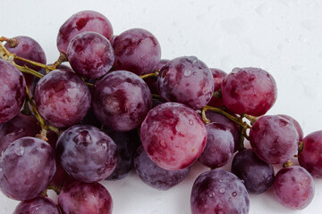 Purple grapes on a white background with drops on the fruits