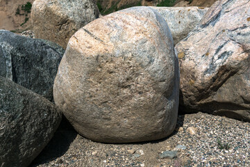 There are big gray stones lying on the sand. The structure of the stone contains inclusions of gray...