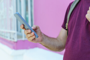 Close up view of unrecognizable man holding a phone on pink background. Horizontal view of man using cellphone isolated on pink wall. People and technology concept.