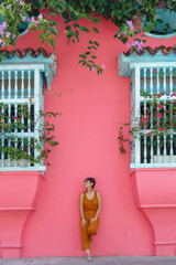 Front view of woman standing on a pink wall with balcony in Cartagena de Indias. vertical view of latin woman sightseeing in spanish historic ancient city. Travel to Colombia concept.