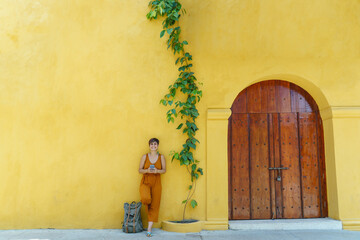 front view of woman standing with smartphone isolated on yellow facade. Horizontal view of latin american woman in front of yellow building. People and colors concept.