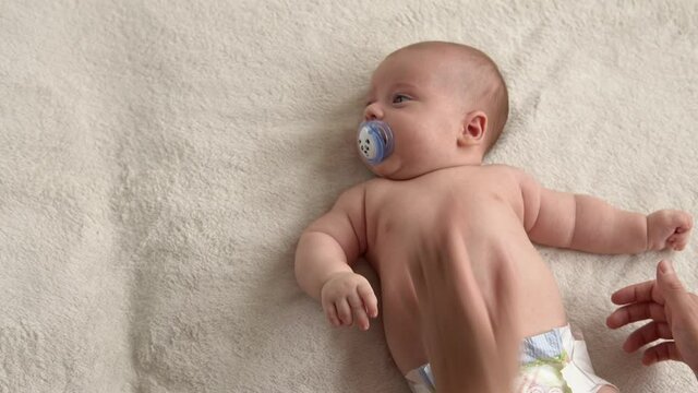 Health skin care, development pediatrics, infant close-up mother hands give naked newborn baby child massage on arms, legs, fingers, reflex on feet exercise, rubbing skin abdomen chest on bed at home