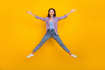 Full length photo of carefree funny lady jump raise hands wear plaid shirt jeans shoes isolated...