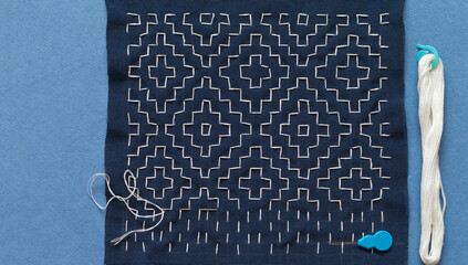 Top view of process of embroidering with white threads on blue fabric in Japanese Sashiko style or...