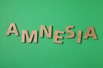 Word Amnesia made of wooden letters on green background, flat lay