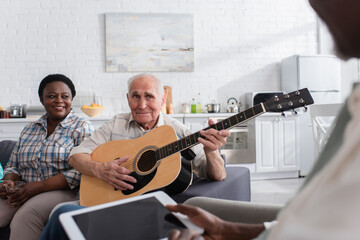 Multiethnic senior people with acoustic guitar and digital tablet in nursing home