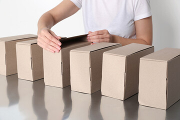 Woman folding cardboard boxes at table, closeup. Production line