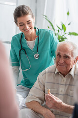 Cheerful nurse in uniform looking at elderly man with chess figure in nursing home