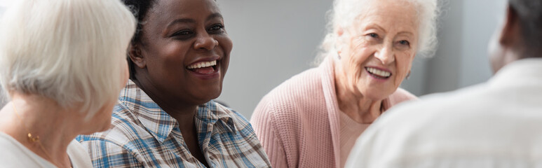 Smiling african american woman talking to elderly friends in nursing home, banner