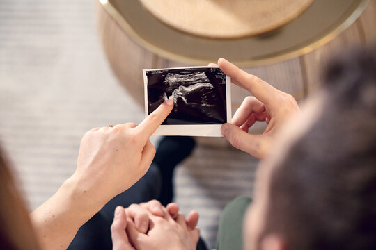 Young pregnant couple holding hands and looking ultrasonic picture