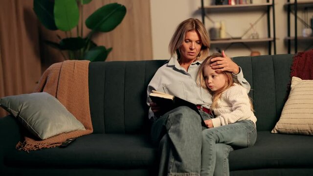 Attractive blond mother and her cute little daughter read children's book together while father with grey hair appears and hug them tightly. Family time. High quality 4k footage