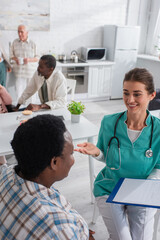 Fototapeta premium Nurse with clipboard talking to african american patient in nursing home