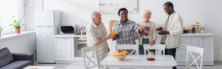 Positive interracial senior people with tea and smartphone in nursing home, banner