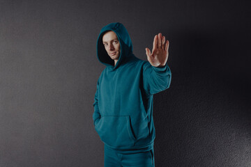 Handsome man wearing green hoodie showing stop sign near wall