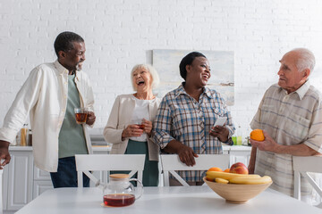 Cheerful multiethnic people holding tea and smartphone while talking in nursing home
