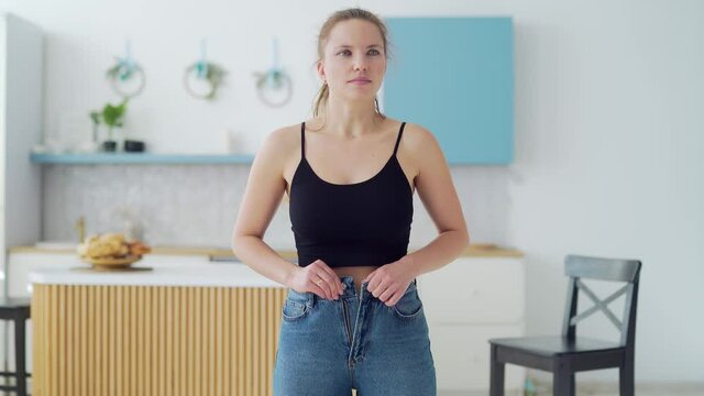 Young fat woman cannot wear small pants after gaining weight. An overweight female tries to button her jeans. Girl with belly getting dressed putting trousers on. Overweight trying to fasten too